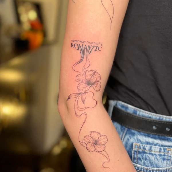 Tekstas „never was much of a ROMANTIC“ su linija ir dviem gėlėmis tattoo ant žasto