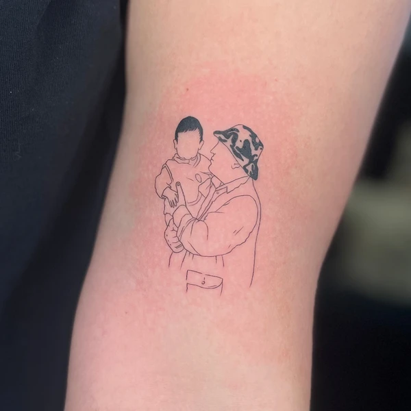 Tėčio laikomo kūdikio linijinė portreto tattoo ant žasto