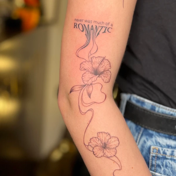 Tekstas „never was much of a ROMANTIC“ su linija ir dviem gėlėmis tattoo ant žasto