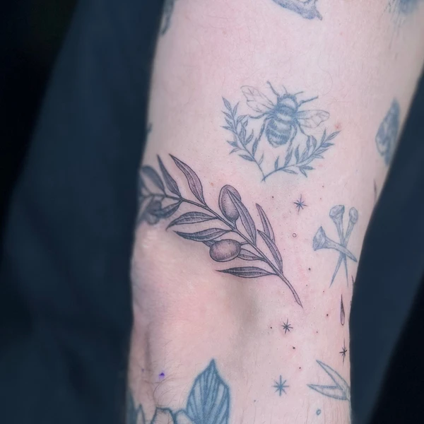 Juodai pilkas alyvmedžio/šakelės motyvas su lapais tattoo ant dilbio