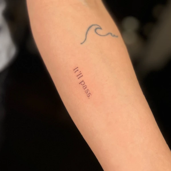 Maža banga ir tekstas „it’ll pass.“ tattoo ant dilbio